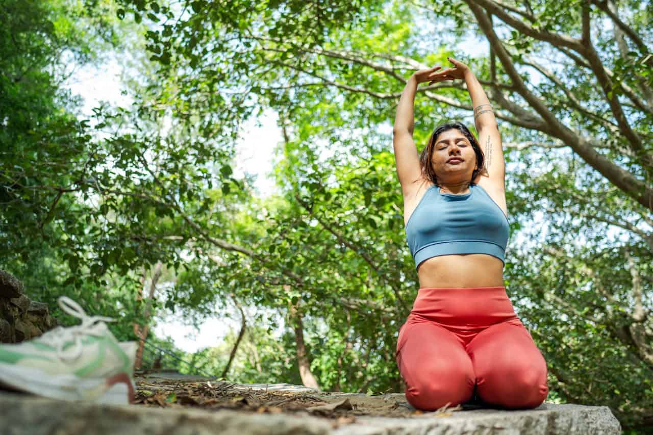 Relaxing woman doing yoga outdoors in lush green forest for wellness and fitness.