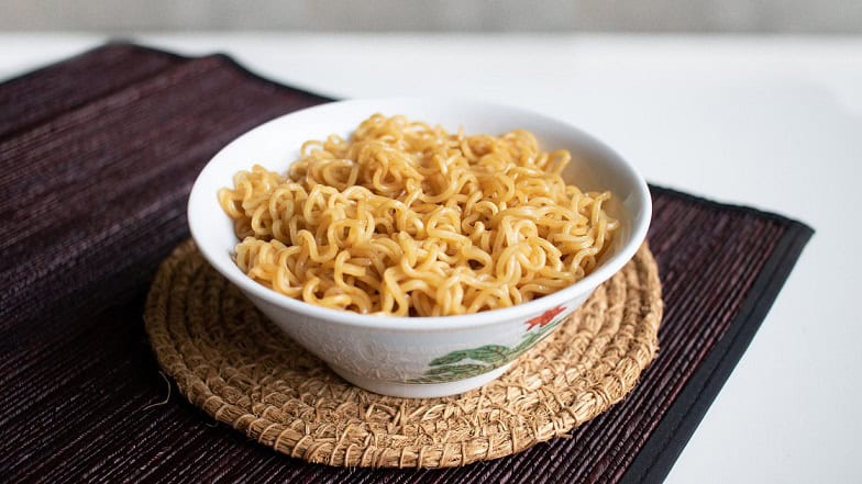 Golden cooked instant noodles in a white bowl on a woven mat, served as quick and easy meal option.