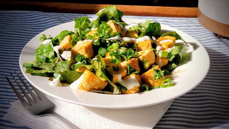 Crispy tofu salad with fresh greens and creamy dressing, served on a white plate. Perfect for healthy dining and vegetarian meals, ideal for food lovers seeking nutritious options.