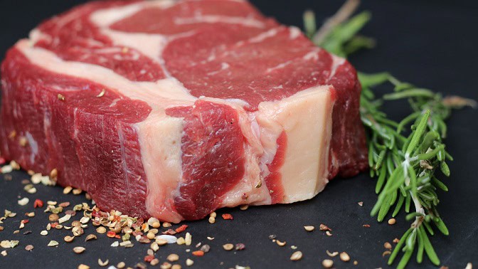 Premium raw beef steak with seasoned spices and fresh herbs on a dark background for high-quality meat products.