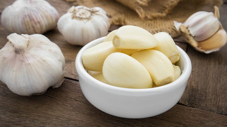 Fresh peeled garlic cloves in a white bowl on rustic wooden background, natural raw garlic for cooking and health benefits.